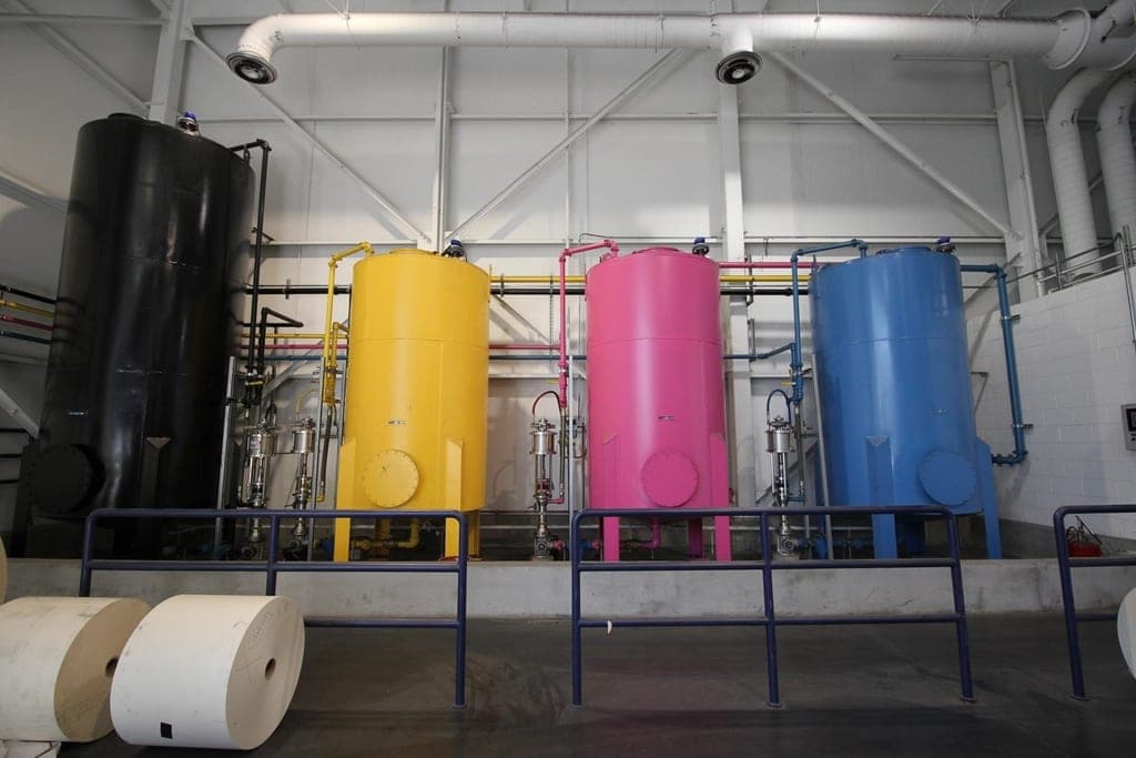 Cyan, magenta and yellow ink tanks next to paper rolls